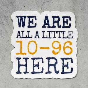May include: A white die-cut sticker with a dark blue and orange graphic design. The text reads WE ARE ALL A LITTLE 10-96 HERE, with the words WE ARE ALL A LITTLE and HERE in dark blue, and the numbers 10-96 in a bold, textured orange font.