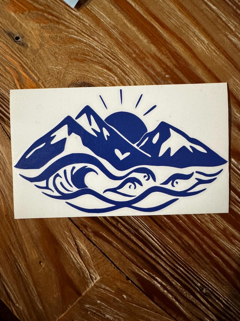 May include: Blue silhouette sticker of mountains, a sun, and waves with a heart in the center.