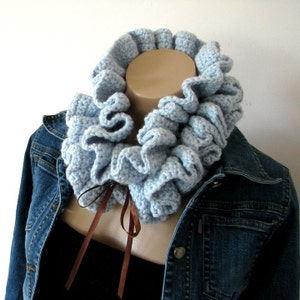 May include: A light blue crocheted ruffle collar with a brown ribbon tied at the front. The collar is worn over a denim jacket.