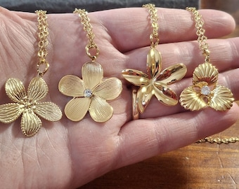 May include: Four gold-tone flower pendant necklaces with clear rhinestone accents. The necklaces feature different flower designs, including a plumeria, a hibiscus, and a daisy.