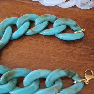 May include: A turquoise blue plastic chain bracelet with a gold clasp. The links of the chain are large and chunky.