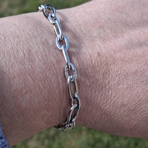 Peut inclure: Un bracelet en argent avec des maillons ovales. Le bracelet est porté au poignet.