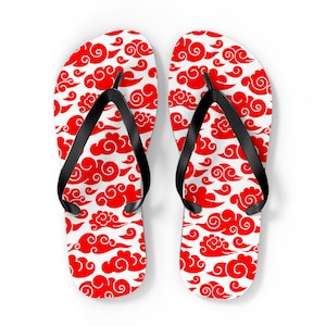 May include: A pair of white flip-flops with a repeating pattern of red cloud designs. The flip-flops have black straps and a white sole. The design is a bold, eye-catching pattern.
