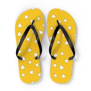 May include: A pair of yellow flip-flops with a repeating pattern of white triangles and vertical lines. The flip-flops have black straps and are set against a white background. These sandals are perfect for casual wear.