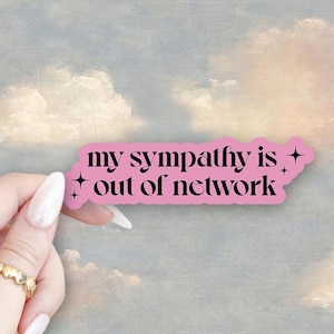 May include: Pink sticker with the text "my sympathy is out of network" with small stars on either side. The sticker is being held by a hand against a background of painted clouds.