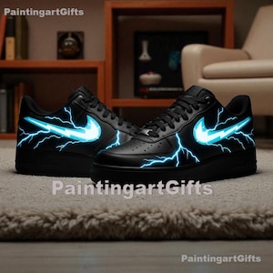 May include: Pair of black sneakers with a white Nike swoosh and blue lightning bolt design. The shoes are displayed on a neutral-colored rug, with a blurred background of furniture.