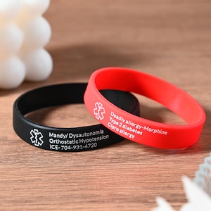 May include: Two silicone medical alert bracelets. The black bracelet has the text "Mandy/Dysautonomia Orthostatic Hypotension ICE-704-931-4720". The red bracelet has the text "Deadly allergy-Morphine Type 2 diabetes Cipro allergy".