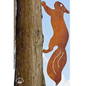 May include: A rusty metal squirrel silhouette climbing a tree trunk. The squirrel is facing right and has a long, bushy tail. The background is a blue sky.