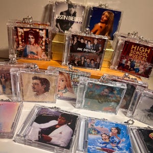 May include: A selection of clear acrylic keyrings displaying album artwork from artists such as Justin Bieber and One Direction. Each keyring has a silver-coloured chain and clasp.