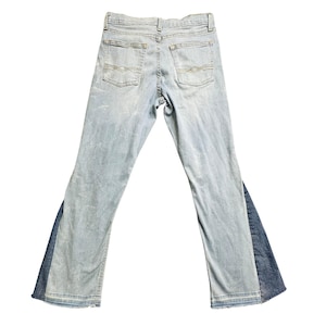 May include: Light blue denim jeans with a contrasting dark blue denim panel on the outer leg. The jeans have a classic five-pocket design, a button and zipper closure, and a faded wash. The back pockets feature a decorative stitch.