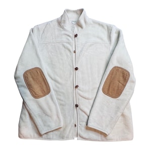 May include: A light beige jacket with a stand-up collar and brown elbow patches. The jacket has a button-up front and brown buttons. The brand name "ORVIS" is visible on the collar. The jacket is made of a soft, textured material.