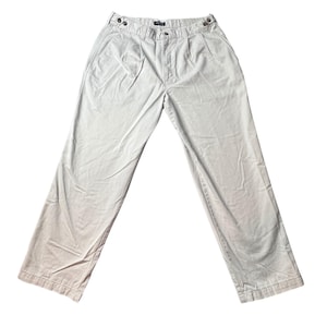 May include: Light beige pleated trousers. These trousers feature a button and zip fastening, belt loops, and two front pockets. They are made from a durable fabric and have a relaxed fit. Suitable for casual or semi-formal occasions. The trousers measure approximately 100 cm in length.