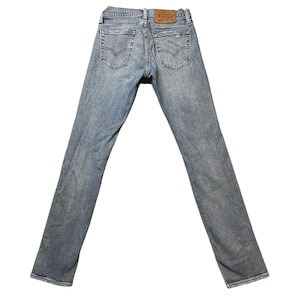 May include: Light blue denim jeans with a faded wash. The jeans feature classic five-pocket styling, a button and zipper closure, and a brown leather patch on the back waistband. The back pockets have a signature stitch design.