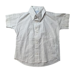 Può includere: Camicia a maniche corte con sottili righe verticali blu su sfondo bianco. La camicia ha un colletto button-down e un piccolo logo sul colletto. Realizzata in tessuto leggero, perfetta per la stagione calda.