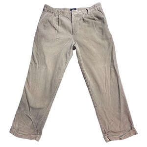 May include: Beige corduroy trousers with a pleated front and turned-up hems. These casual trousers have a classic design, suitable for various occasions. The fabric appears soft and comfortable, with a subtle sheen. The trousers are a neutral colour, making them versatile for different outfits.