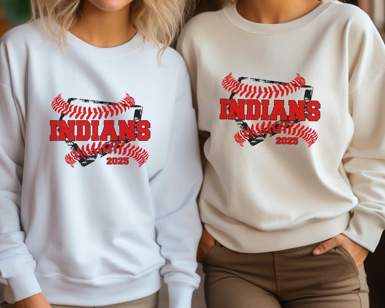 May include: Two white sweatshirts with a baseball-themed graphic. The graphic features a red baseball diamond with the word "INDIANS" in red text and the year "2023" in black text. The diamond is surrounded by red and black baseball stitching.