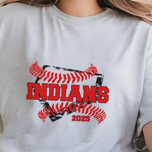 May include: A white t-shirt with a red and black baseball graphic. The graphic features a baseball diamond with the word "INDIANS" in red text and the year "2025" in black text.