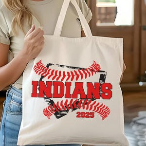 May include: White canvas tote bag with a red and black baseball graphic. The graphic features a baseball with red stitching and the text "INDIANS 2023".