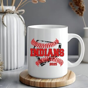 May include: White ceramic mug with a red and black baseball graphic. The graphic features a baseball with red stitching and the word "INDIANS" in red text. The year "2025" is also included in the graphic.