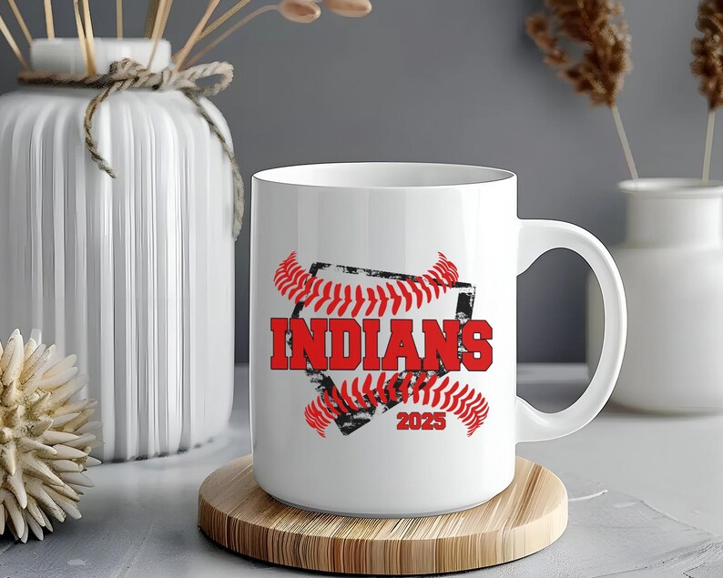 May include: White ceramic mug with a red and black baseball graphic. The graphic features a baseball with red stitching and the word "INDIANS" in red text. The year "2025" is also included in the graphic.