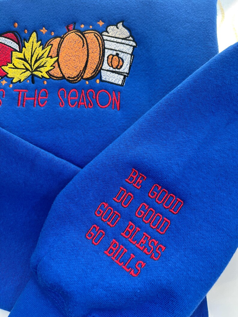 May include: Royal blue sweatshirt with embroidered fall-themed design. Features pumpkins, a leaf, and a coffee cup with the text "'Tis the Season". The sleeve has the text "Be Good, Do Good, God Bless, Go Bills".