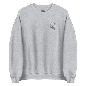 Puede incluir: Sudadera gris claro con cuello redondo. Presenta un pequeño gráfico en blanco y negro de una taza de café en la parte delantera, con el texto "Running on Coffee and Data" debajo. La sudadera está hecha de un material suave.
