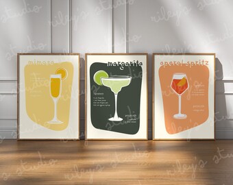 May include: Three framed art prints featuring cocktail recipes. The prints showcase a Mimosa, Margarita, and Aperol Spritz, each with a stylized illustration of the drink and its ingredients. The color palette includes yellow, green, and orange hues.