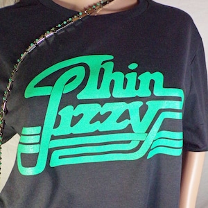 May include: A black t-shirt with a green graphic that says "Thin Lizzy" in a retro font.