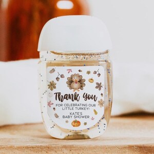 May include: A clear hand sanitizer bottle with a white cap and a label that reads "Thank you" with a turkey illustration. The label also says "For celebrating our little turkey!" and "Kate's baby shower."