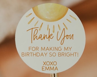 May include: A round, white thank you sticker with a yellow sun graphic and the text "Thank You" in brown. The sticker also says "For making my birthday so bright! XOXO Emma".