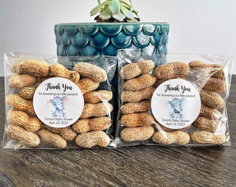 May include: Two clear plastic bags filled with peanuts, each with a round thank you sticker. The sticker features a cartoon elephant with a blue and gray color scheme and the text "Thank You for showering our little peanut! Tonya's Baby Shower April 10, 2022".