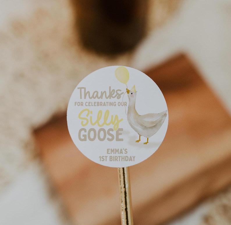 May include: Round white sticker with a yellow balloon, a white goose with a yellow crown, and the text "Thanks for celebrating our Silly Goose Emma's 1st Birthday".