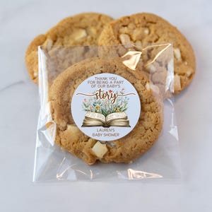 May include: A clear plastic bag filled with cookies. A round sticker with a blue background and a book with flowers on it says "Thank you for being a part of our baby's story."  The sticker also says "Lauren's Baby Shower".