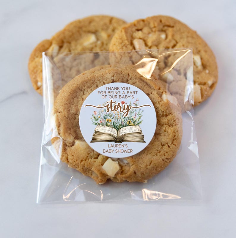May include: A clear plastic bag filled with cookies. A round sticker with a blue background and a book with flowers on it says "Thank you for being a part of our baby's story."  The sticker also says "Lauren's Baby Shower".