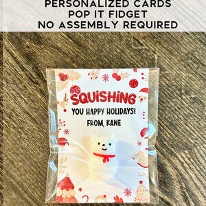 May include: A white pop it fidget toy in the shape of a polar bear with a red scarf. The toy is packaged in a clear plastic bag with a white card that says "Squishing You Happy Holidays! From, Kane".