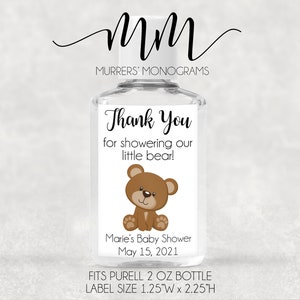 May include: A white label with brown text that says "Thank You for showering our little bear!" with a cartoon brown bear illustration. The label is attached to a clear plastic bottle of hand sanitizer. The label also includes the text "Marie's Baby Shower May 15, 2021". The label is 1.25 inches wide by 2.25 inches high and fits a 2 ounce Purell bottle.