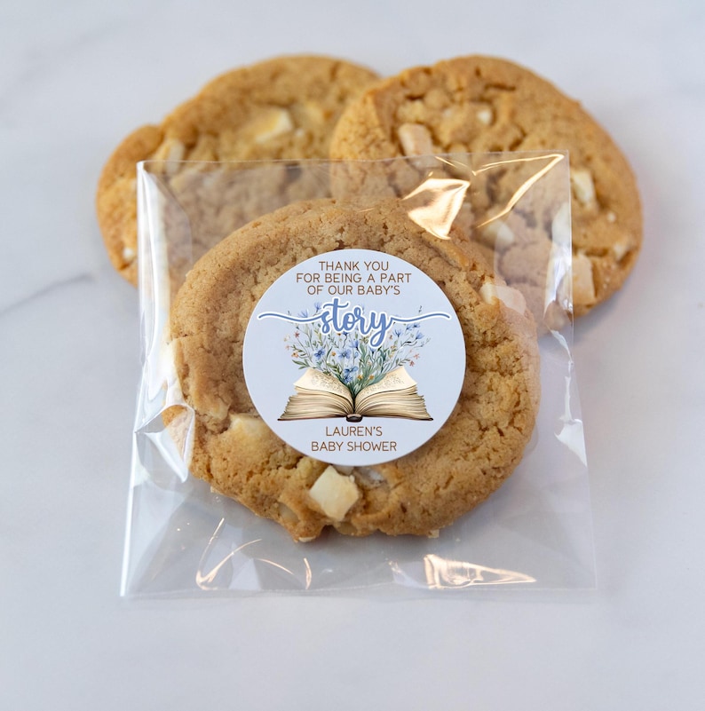 May include: A blue and white book with flowers on the cover. The book is open and the text "Thank you for being a part of our baby's story" is visible. The sticker is on a clear plastic bag with cookies inside. The text "Lauren's Baby Shower" is also visible on the sticker.