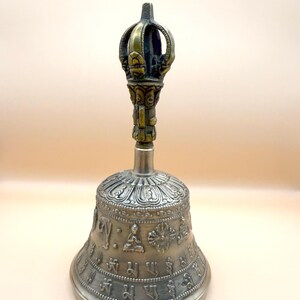 May include: A silver bell with intricate carvings and a golden handle. The bell is decorated with Buddhist symbols and mantras.