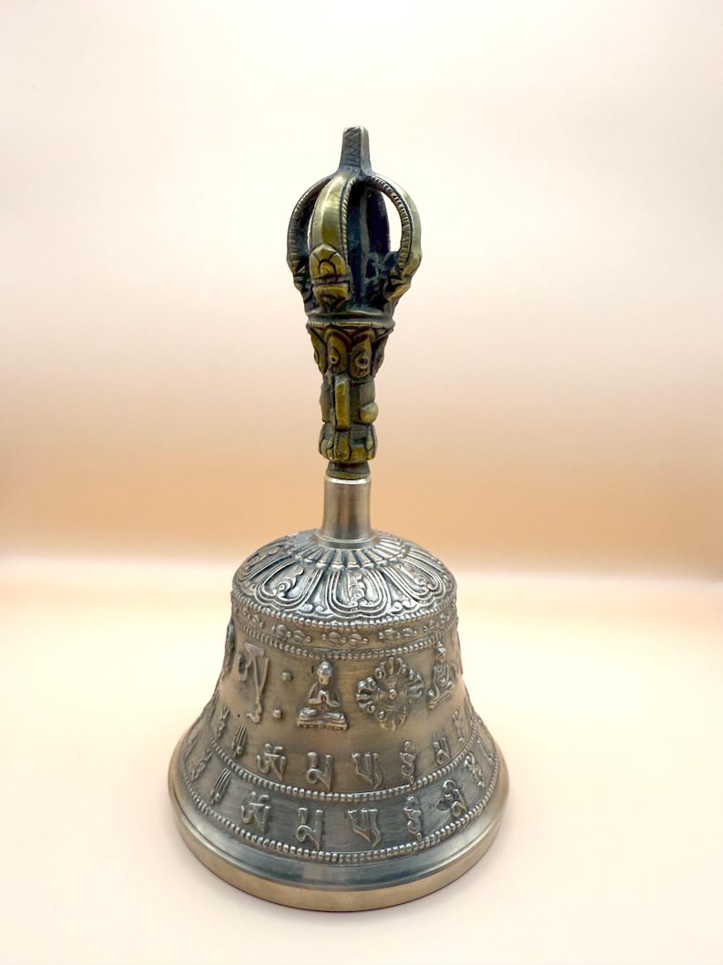 May include: A silver bell with intricate carvings and a golden handle. The bell is decorated with Buddhist symbols and mantras.