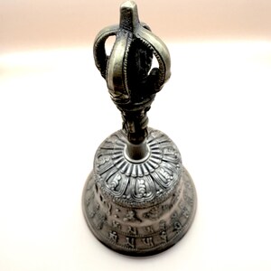 May include: A silver bell with intricate carvings and a decorative handle. The bell has a crown-like top and is adorned with ornate designs.