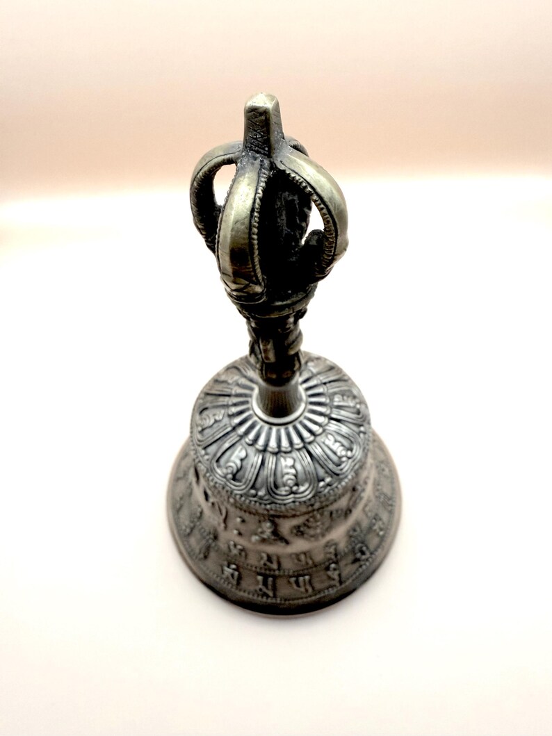 May include: A silver bell with intricate carvings and a decorative handle. The bell has a crown-like top and is adorned with ornate designs.
