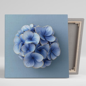 May include: A canvas print featuring a close-up of a blue hydrangea flower with gold-colored edges. The flower is centered on a light blue background. The canvas is stretched over a wooden frame.
