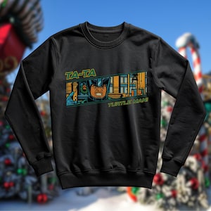 May include: Black sweatshirt with a comic book-style graphic. The graphic features a character in a helmet with the text "TA-TA TURTLE MAN!" in green and yellow. The character is pointing with an angry expression.