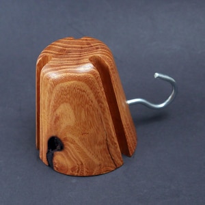 May include: A wooden hat stand with a metal hook. The stand is made of light brown wood with a dark brown stain. The hook is silver and is attached to the side of the stand.