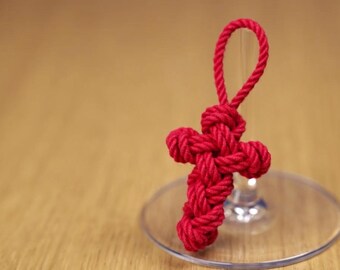 May include: A red rope tied into a cross shape, hanging from a glass wine glass.