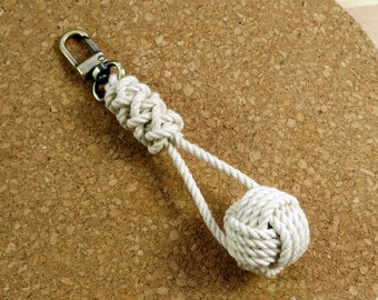 May include: A white rope keychain with a knot at the end. The keychain is attached to a metal ring.