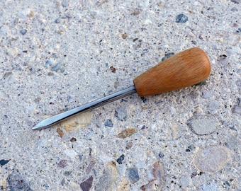 May include: An ice pick with a wooden handle and a pointed metal tip. The handle is a light brown color, and the metal portion is silver. The tool is designed for piercing ice or other materials.
