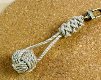 May include: A beige rope keychain with a knotted ball at the end and a brass key ring.