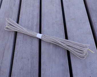 May include: A bundle of natural beige twine, tied together with a white label, on a wooden surface.