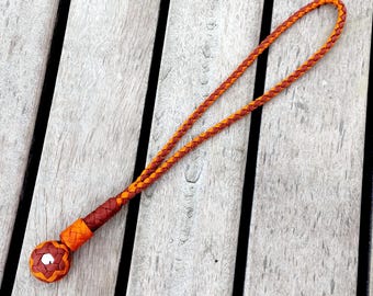 May include: A handcrafted lanyard featuring a braided orange and brown cord. The lanyard has a decorative, spherical end with a woven pattern and a loop for attaching keys or other small items. The design is symmetrical and the colors are vibrant.